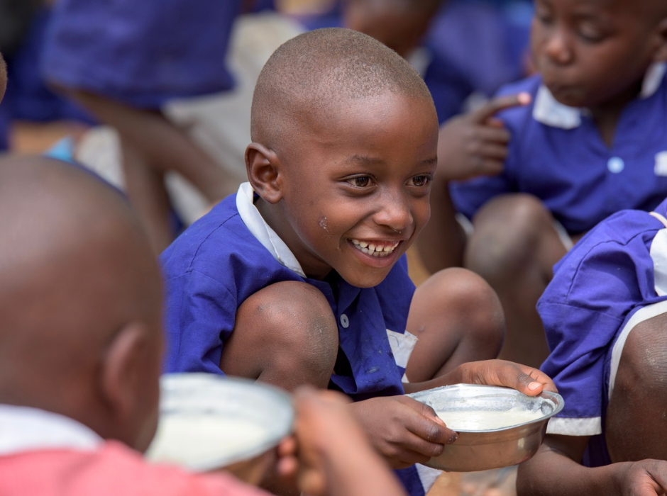 smiling child holding a bowl with their meal provided at school