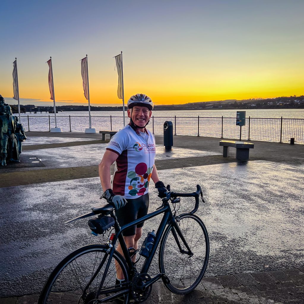 male cyclist standing next to bike smiling with sunset behind